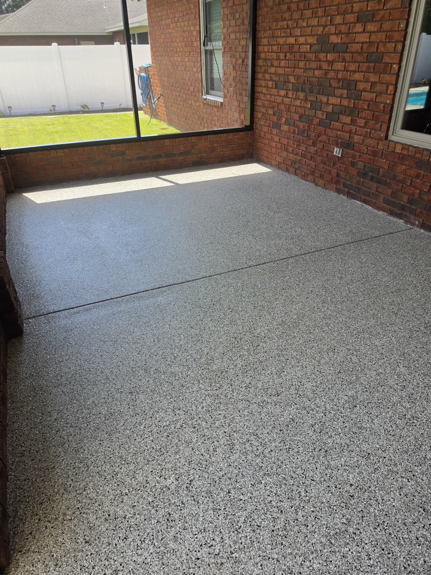 Finished flake coating on a covered patio with brick walls and a screened yard